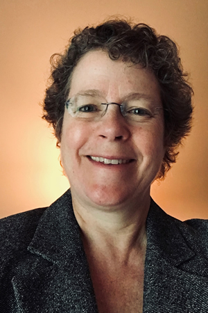 Dressed in a business suit a woman with glasses smiles at the camera.